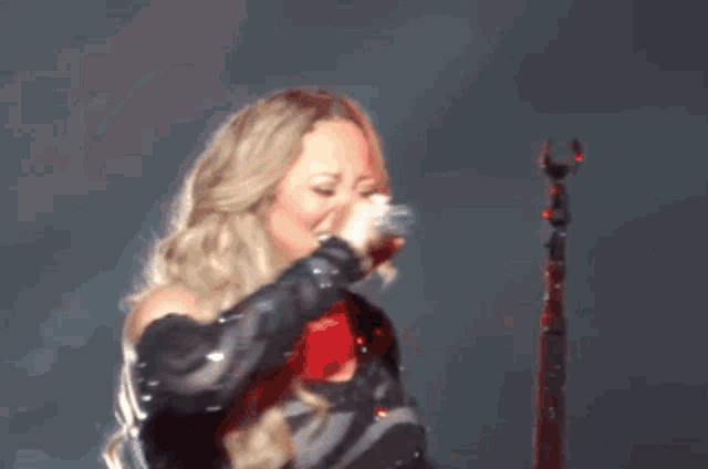 a blonde woman singing into a microphone with a red light behind her