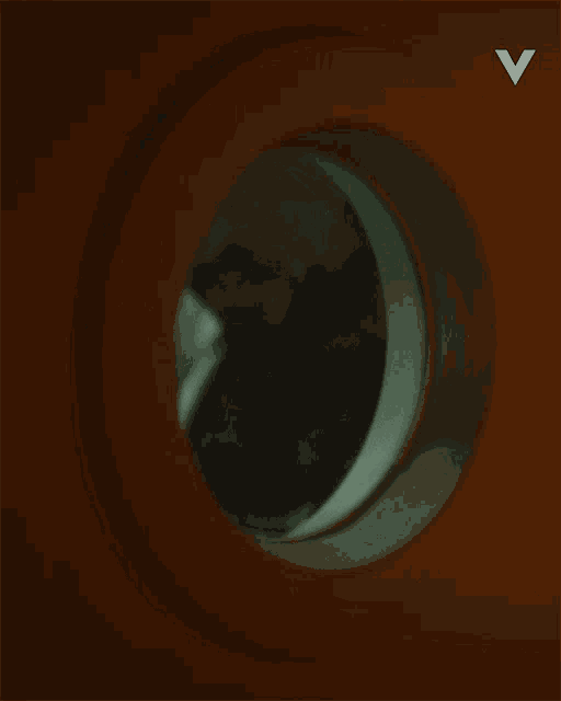 a man 's face is visible through a round window with the letter v above it