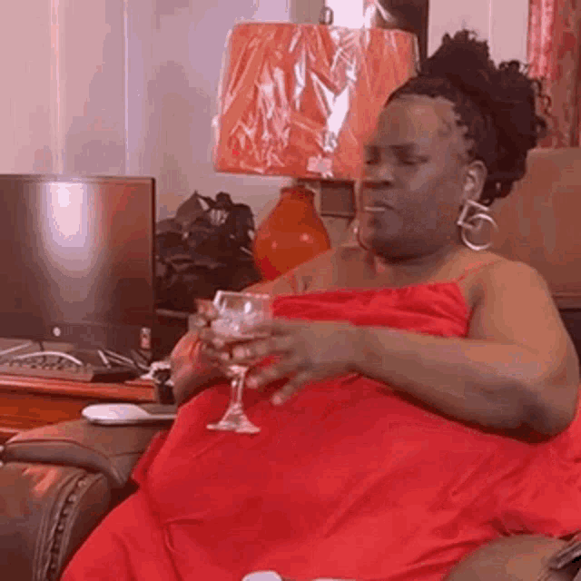 a very fat woman in a red dress is sitting in a chair holding a glass of wine .