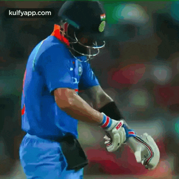 a cricket player wearing a helmet and gloves with a kulfyapp.com logo on the bottom