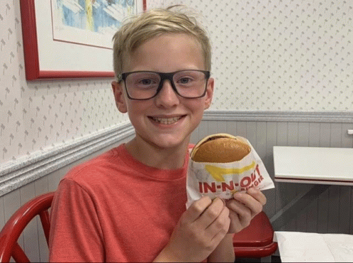 a young boy wearing glasses is holding a in-n-out hamburger