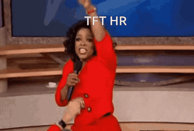 a woman in a red dress is holding a microphone and the words tft hr are on the screen behind her
