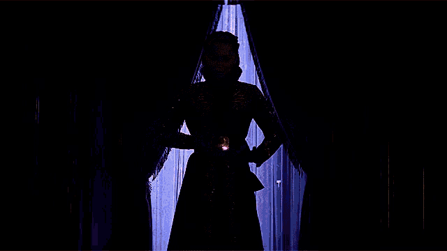 a woman in a black and gold dress is holding a glowing object in her hands