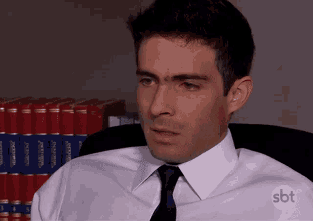 a man wearing a white shirt and tie is sitting in front of a shelf of books .