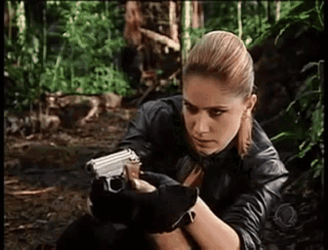 a woman is holding a gun in a forest .