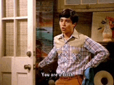 a man in a plaid shirt is standing in front of a door with his hands on his hips .