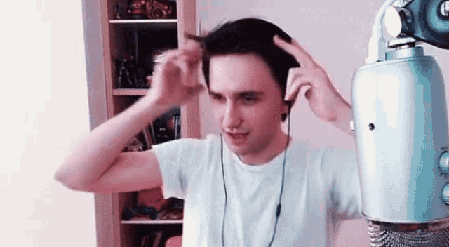 a young man wearing headphones and a white shirt is standing in front of a blue microphone .