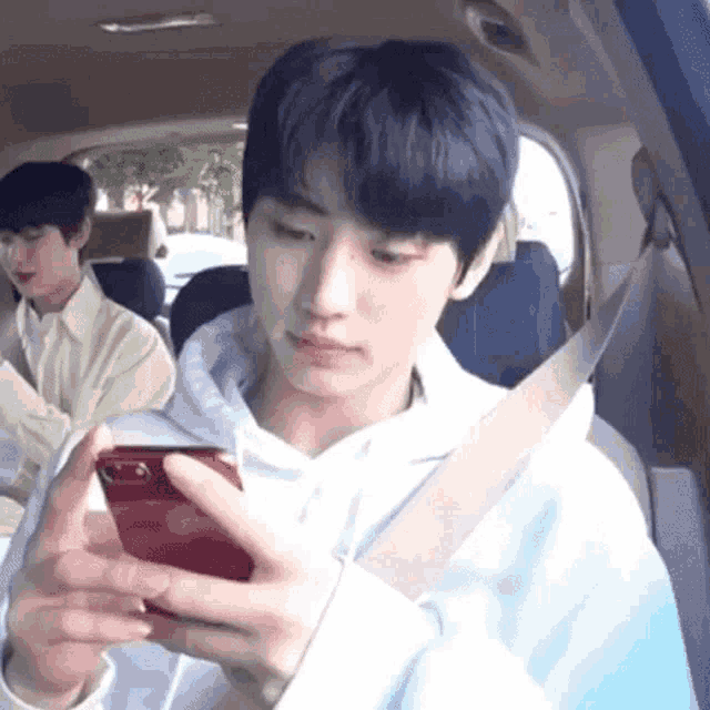a young man is sitting in a car looking at his cell phone .