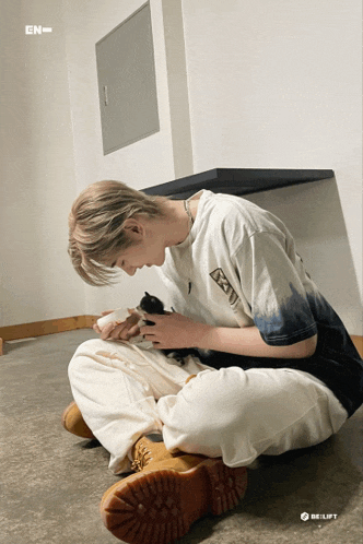a man is sitting on the floor holding a kitten and wearing a t-shirt that says en on it