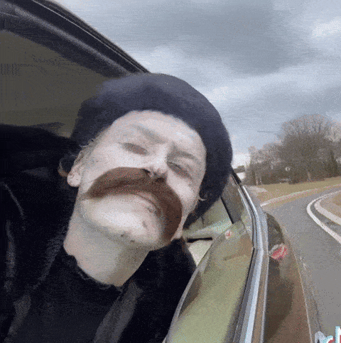 a man with a mustache is looking out of a car window