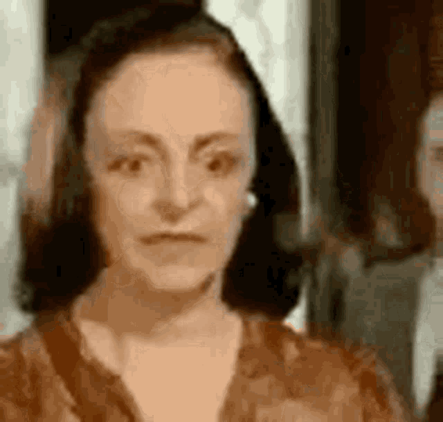 a woman in a brown dress is looking at the camera with a man in a suit in the background .