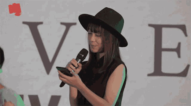a woman wearing a black hat is looking at her phone in front of a sign that says ve