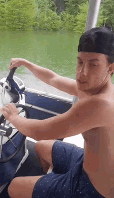 a shirtless man is sitting on a boat holding the steering wheel