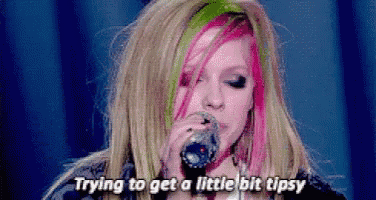 a woman with pink and green hair is singing into a microphone and saying " trying to get a little bit tipsy " .