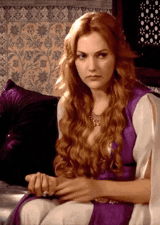 a woman with long red hair is sitting on a couch in a purple dress .
