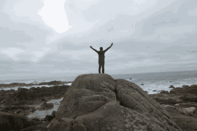 a person standing on top of a large rock with their arms outstretched