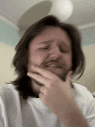 a man with long hair and a beard is covering his face with his hand