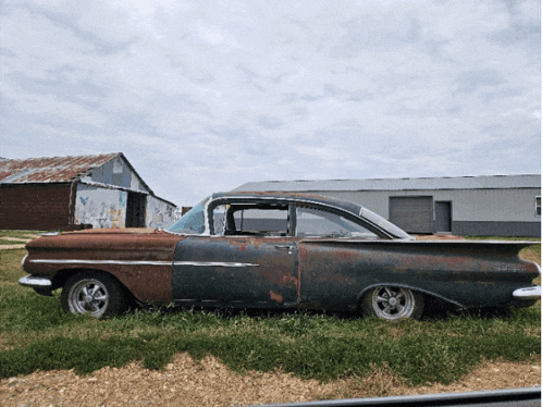 an old rusty car is parked in a field with a barn in the background