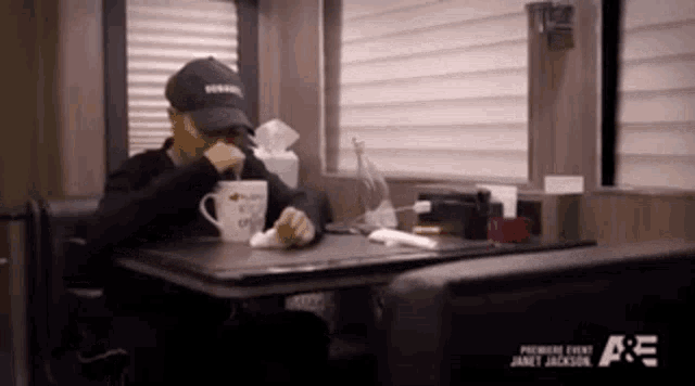 a man in a hat sits at a table with a cup that says " i love you " on it
