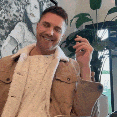 a man wearing a tan jacket is smiling with his eyes closed