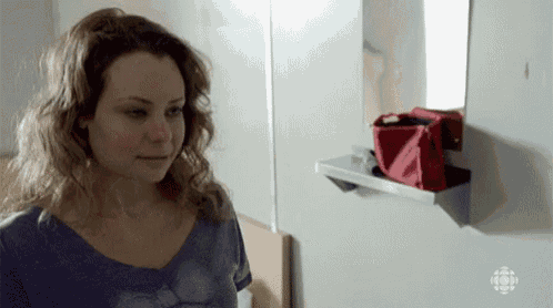 a woman stands in front of a mirror with a red bag on a shelf