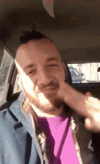 a man with a beard is sitting in the back seat of a car holding a piece of paper to his face .
