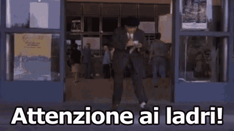 a man in a suit is dancing in front of a building with the words attentione ai ladri .