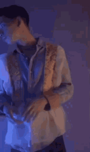 a man is standing in a dark room with a purple light behind him and his arms crossed .