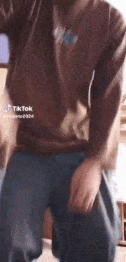 a man in a brown shirt and blue pants is dancing in a room .