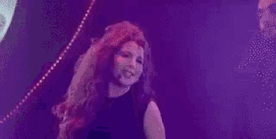 a woman with long red hair is dancing on a stage in front of a purple light .