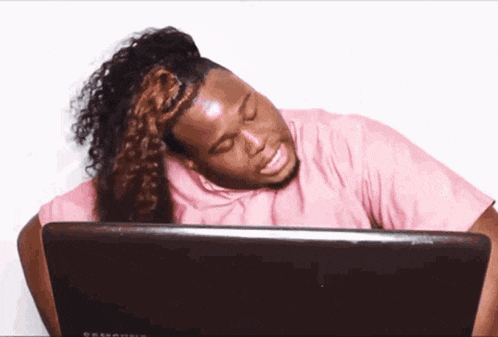 a man in a pink shirt is looking at a laptop