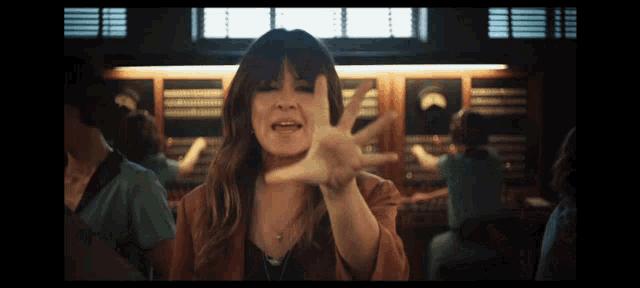 a woman in a brown jacket is making a funny face with her hand