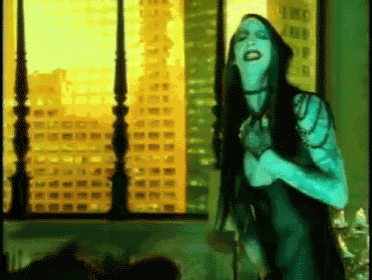 a woman with long black hair is standing in front of a window with a city in the background .