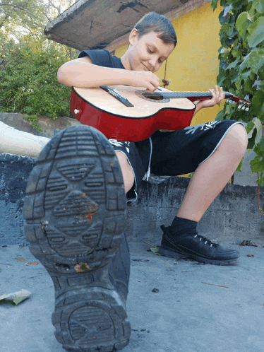 a boy playing a guitar with a shoe in the foreground that says reebok