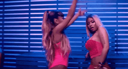 ariana grande and nicki minaj are dancing in front of a wooden wall .