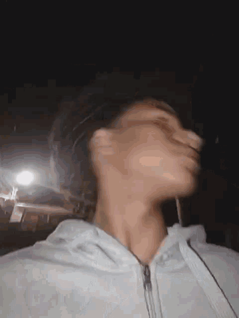 a man in a white hoodie is taking a picture of himself in the dark .