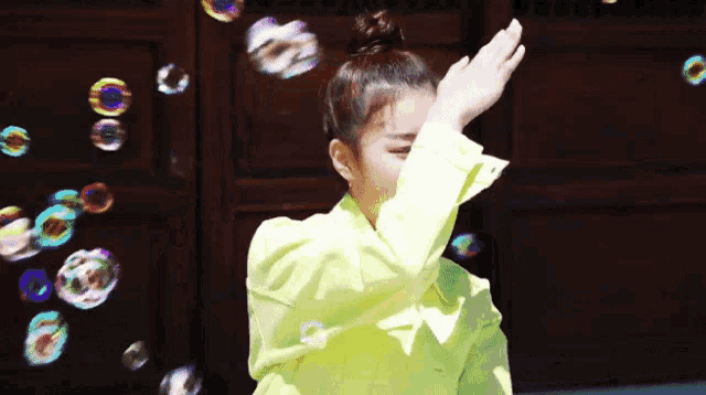 a woman in a yellow jacket is blowing soap bubbles .