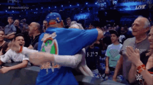 a man in a blue shirt with a rainbow on the back is standing in front of a crowd at a wrestling match .