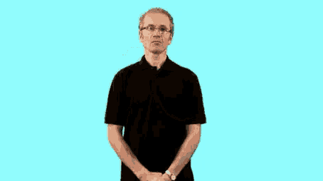 a man wearing glasses and a black shirt is making a hand gesture with his hands .