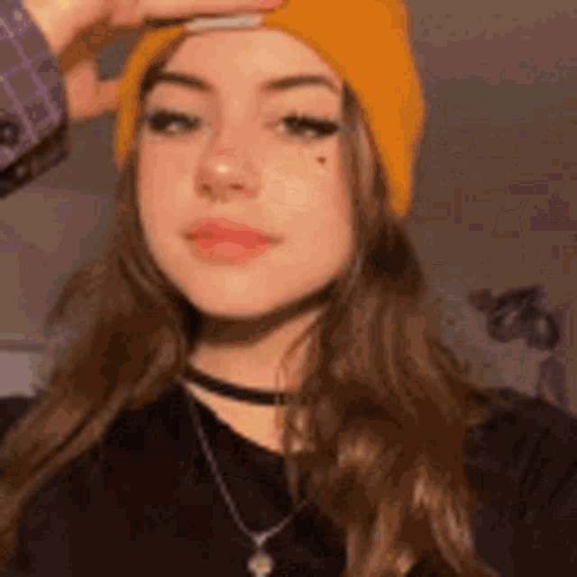 a girl wearing a yellow beanie and a choker is looking at the camera .