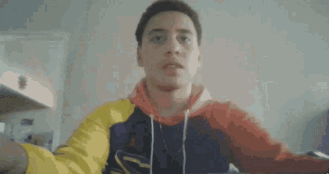 a young man in a colorful hoodie is taking a selfie with his phone .