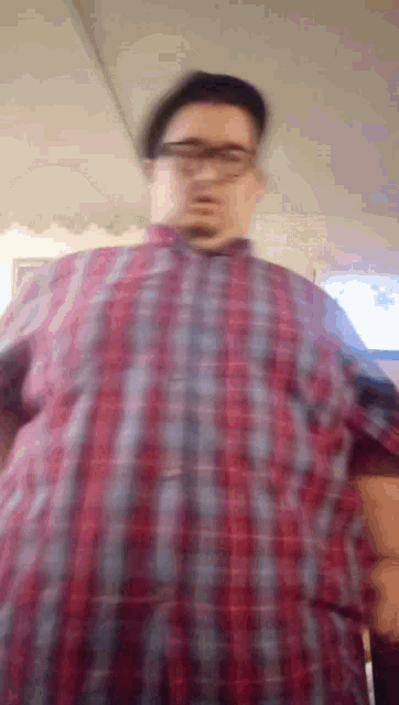 a man wearing glasses and a plaid shirt is taking off his shirt