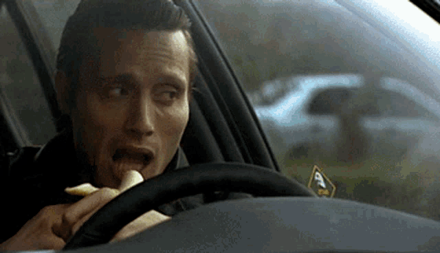 a man is eating a banana while driving a car with a sticker on the windshield that says ' a '