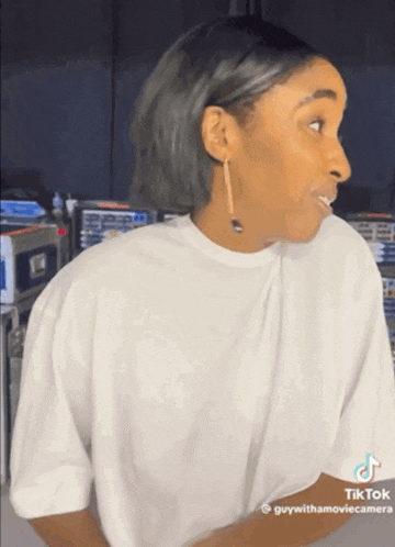 a woman wearing a white t-shirt and gold earrings is making a funny face
