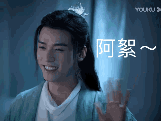 a young man in a green kimono is smiling and waving his hand in front of a youku logo