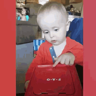 a baby is playing with a red container that says f-a-o