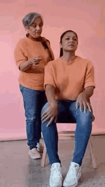 a woman is standing next to a woman sitting in a chair and talking to her .