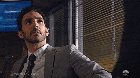 a man in a suit and tie is standing in front of a window with blinds on it ..
