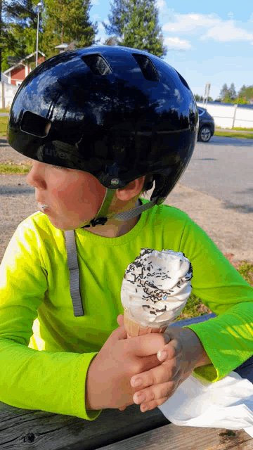 a young boy wearing a black helmet holds an ice cream cone in his hands