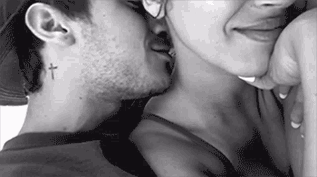 a man and a woman are kissing with a cross tattoo on the back of his neck .
